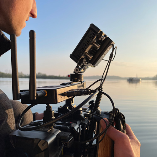 Videograaf met camera op boot in het water. Jacht in de achtergrond.